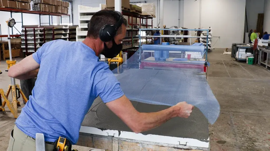 Fabricator applying reinforcing mesh on wall panel.