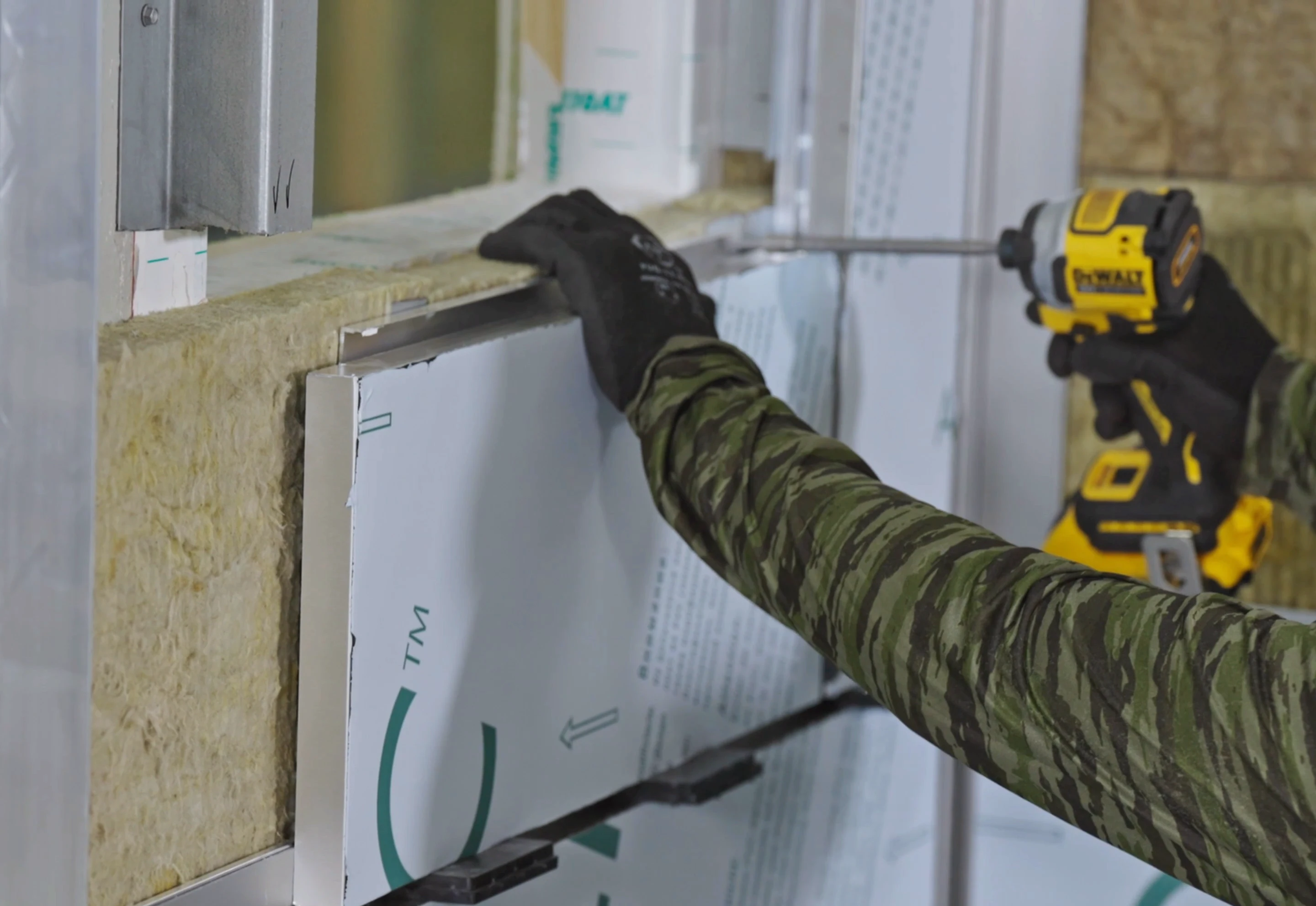 Worker screwing metal panel to exterior framing.